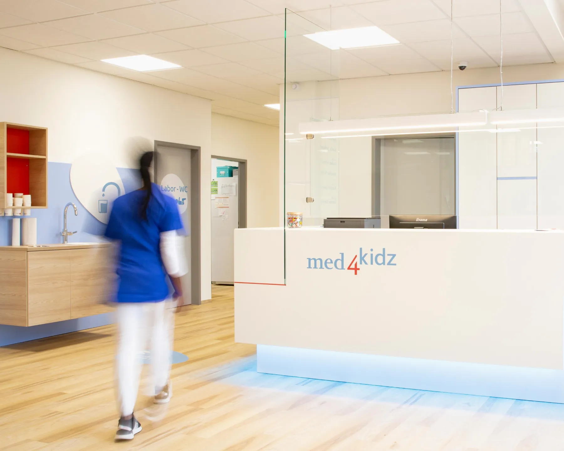 Praxismitarbeiterin am modernen Empfangstresen mit dem med4kidz Markenlogo.
